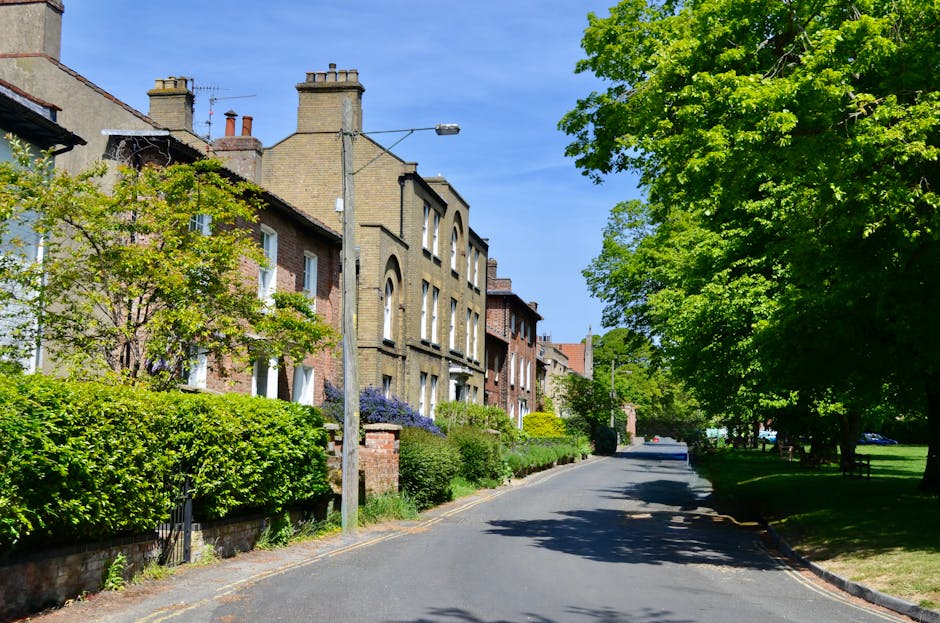 A peaceful residential street in Hampstead Garden Suburb with a row of Victorian-style terraced houses on the left, featuring brick facades, tall chimney stacks, and arched windows. The houses are par